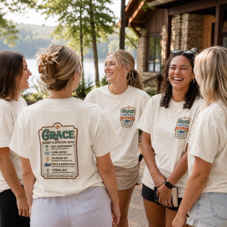 Puede incluir: Un grupo de personas con camisetas color crema. La parte delantera de las camisetas muestra "Grace Motel" en un dise&ntilde;o vintage. La parte trasera de las camisetas presenta "Grace Resort & Spiritual Oasis". El dise&ntilde;o tiene detalles en verde y marr&oacute;n. La gente sonr&iacute;e y r&iacute;e.
