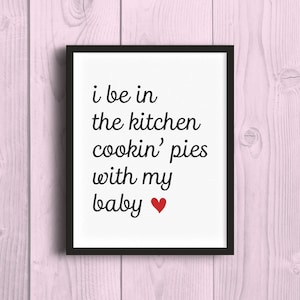 以下が含まれることがあります： 白い背景に黒い文字で「i be in the kitchen cookin' pies with my baby」と書かれた黒い額縁のプリント。赤いハートマーク付き。