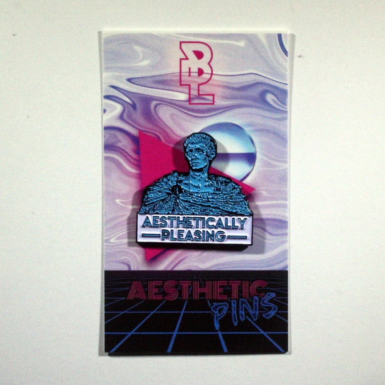 May include: Aesthetic pin featuring a blue bust with the text "Aesthetically Pleasing" on a white banner. The pin is on a card with a vaporwave design and the words "Aesthetic Pins".