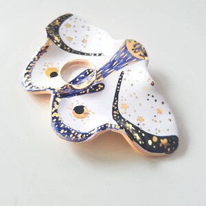 May include: White ceramic ring dish shaped like a butterfly with blue and gold accents. The butterfly has a gold ring holder in the centre.