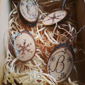 May include: Four wooden ornaments with a snowflake design and the letters "E" and "B" burned into the wood. The ornaments are in a box with shredded paper.