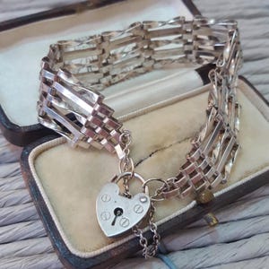 May include: A silver chain bracelet with a heart-shaped padlock charm. The bracelet is made of multiple interwoven strands of silver.