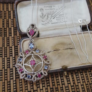 May include: A white ceramic mug with a black handle and the text "But First, Coffee" in a bold, black font. The mug is set against a blurred background, suggesting a cosy setting.