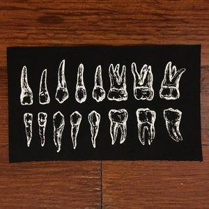 May include: Black fabric patch with white embroidered images of different types of teeth.