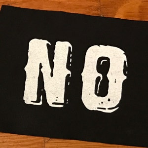 Pode incluir: Remendo de tecido preto com a palavra "NO" impressa em branco.