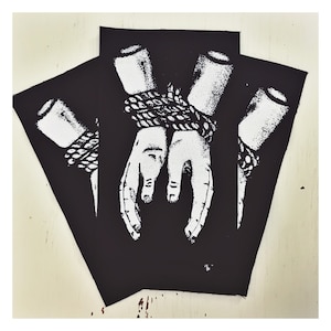 May include: Three black fabric patches featuring a white design of two hands bound together with rope. The hands are shown in close-up and the rope is tied tightly around the wrists.