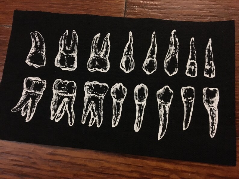 Peut inclure: Un patch en tissu noir avec un contour blanc de diff&eacute;rents types de dents. Les dents sont dispos&eacute;es sur deux rang&eacute;es.