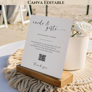 Könnte beinhalten: Eine weiße Karte mit dem Text "cards & gifts" und einem QR-Code, die auf einem Holzständer präsentiert wird. Die Karte enthält auch den Text "With heartfelt thanks" und "thank you". Eine weiße Vase mit einer weißen Rose ist sichtbar.