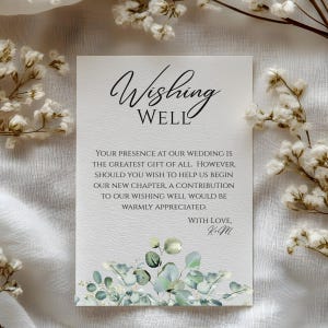 May include: A rectangular wedding wishing well card with the words "Wishing Well" in elegant script. The card includes a message about contributions and is decorated with floral elements.