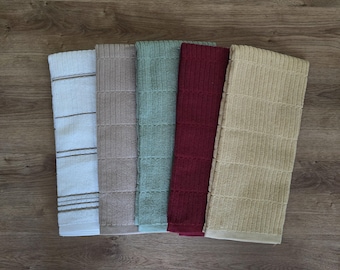 May include: A collection of five kitchen towels in various colors, including white with brown stripes, taupe, teal, burgundy, and beige. Each towel has a textured, ribbed design. The towels are arranged on a wooden surface.