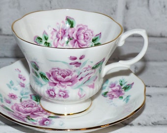 May include: A white teacup and saucer with a floral pattern featuring pink and green roses. The cup has a gold rim and a delicate handle.