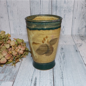 May include: A ceramic vase with a green and brown glaze. The vase has a wide mouth and a narrow base. It is decorated with a floral pattern.