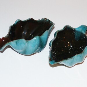 May include: Two teal blue and brown ceramic leaf-shaped bowls. The bowls have a glossy finish and are perfect for serving small snacks or dips.