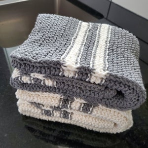 May include: A stack of three knitted dishcloths. The top dishcloth is gray with white stripes. The bottom two dishcloths are white with gray stripes.