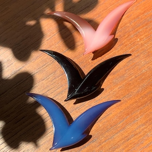 May include: Three seagull-shaped hair clips in different colours: pink, black and blue.