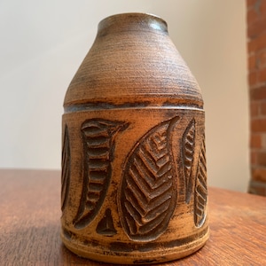 May include: A brown ceramic vase with a leaf design. The vase is approximately 15 cm tall and has a wide mouth.