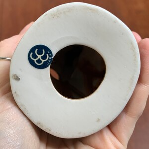 May include: White ceramic figurine with a blue and white sticker on the bottom that reads "JAPAN" and has a triple C logo. The figurine has a hole in the bottom.