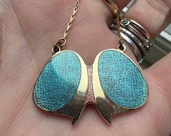 May include: A gold-toned pendant featuring two symmetrical, textured turquoise enamel sections separated by a central vertical strip of pink glitter. The pendant is suspended from a delicate gold-toned chain and has a smooth, polished gold-toned border.