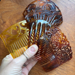 Könnte beinhalten: Eine Sammlung von Vintage-Haarkämmen in Bernstein- und Honigtönen. Die Kämme weisen aufwendige Schnitzereien auf, darunter florale und geometrische Muster. Die Kollektion umfasst eine Vielzahl von Formen und Größen, die die Handwerkskunst der Epoche zeigen.