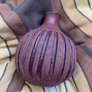May include: A dark purple ceramic vase with a ribbed design. The vase has a rounded body and a narrow neck.