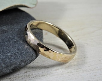 May include: A simple gold band ring with a hammered texture. The ring is shown on a gray stone background.