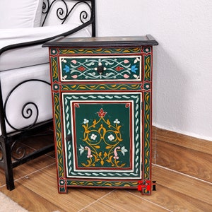 May include: A hand-painted wooden nightstand with a drawer and cabinet door. The nightstand features intricate floral designs in green, red, yellow, and white against a dark green background. The top is black with floral accents, and the hardware is black.