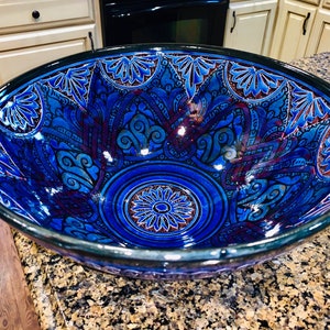 May include: A decorative ceramic bowl with a deep blue glaze and intricate floral and paisley patterns. The bowl's interior features a central floral design and is trimmed with a dark blue border. The bowl is approximately 12 inches in diameter.