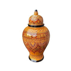 May include: A decorative ceramic jar with a lid. The jar is primarily yellow with intricate orange and black geometric patterns. The lid is topped with a small black knob. The jar has a glossy finish and a wide base.