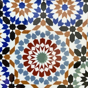 May include: A white ceramic tile with a geometric pattern in shades of blue, brown, red, and green. The pattern is made up of repeating shapes, including stars, diamonds, and circles.
