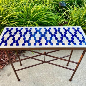 May include: A small, white and blue tiled table with a brown metal frame. The table has a geometric pattern of hexagons.