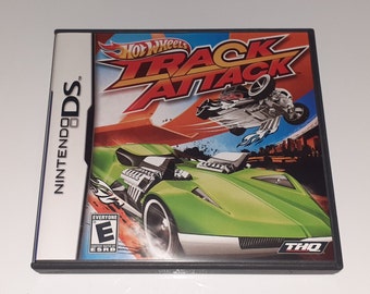 May include: A Nintendo DS game case for Hot Wheels Track Attack. The cover features a green sports car and a car in mid-air, with the game's title in red and orange. The case is labeled "Everyone" by ESRB.