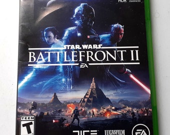 May include: Xbox One video game case for Star Wars Battlefront II, featuring a green background with the game title and logos for EA, DICE, and Lucasfilm. The front cover shows characters from the game, including Darth Vader, Iden Versio, and a Rebel soldier.