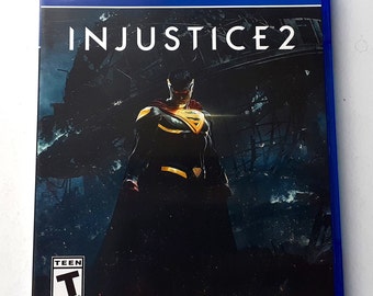 May include: A blue PlayStation 4 game case with a dark background image of Superman in a black and yellow suit. The game title "INJUSTICE 2" is printed in white on the case. The ESRB rating of "T" for Teen is displayed in the lower left corner.