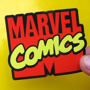 May include: A red and yellow sticker with the text "MARVEL COMICS" in a bold, comic book style font.