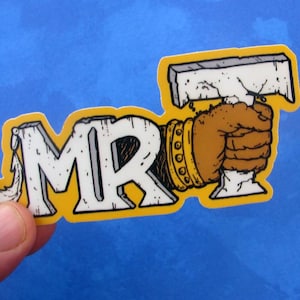 Könnte beinhalten: Ein Aufkleber mit den Buchstaben "MR" in Weiß auf gelbem Hintergrund. Das Design zeigt eine braune Hand, die eine Kelle hält. Die Hand trägt ein goldenes Armband.