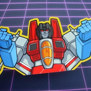 Puede incluir: Una pegatina de vinilo troquelada con una ilustración de dibujos animados del personaje Starscream de Transformers. El robot se muestra con un esquema de colores rojo, blanco y azul, cabeza negra y ventana de cabina naranja con borde amarillo.