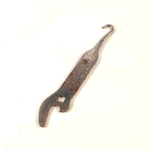 Könnte beinhalten: Ein verrostetes, vintage Metallwerkzeug mit einem Haken an einem Ende und einer quadratischen Öffnung und einem gebogenen Ende am anderen. Das Werkzeug hat eingestanzten Text. Es wird wahrscheinlich für eine mechanische Aufgabe verwendet.