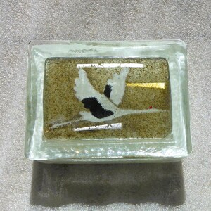May include: A rectangular glass paperweight with a painted image of a bird in flight. The bird is white and black against a tan background with a gold accent. The paperweight is clear with a rectangular shape.
