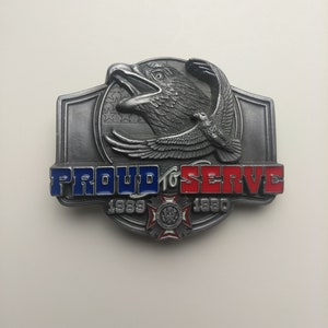May include: A silver belt buckle with an eagle design and the words "Proud to Serve 1989-1990".