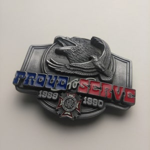 May include: A silver belt buckle with a red, white, and blue eagle design. The buckle says "Proud to Serve 1989-1990".