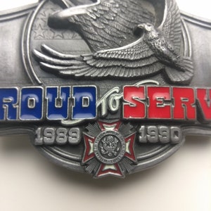 May include: A silver belt buckle with a bald eagle design and the words "Proud to Serve" in red, white, and blue. The buckle also features a red, white, and blue cross with the words "Foreign Wars of the United States" and the years "1989" and "1990".