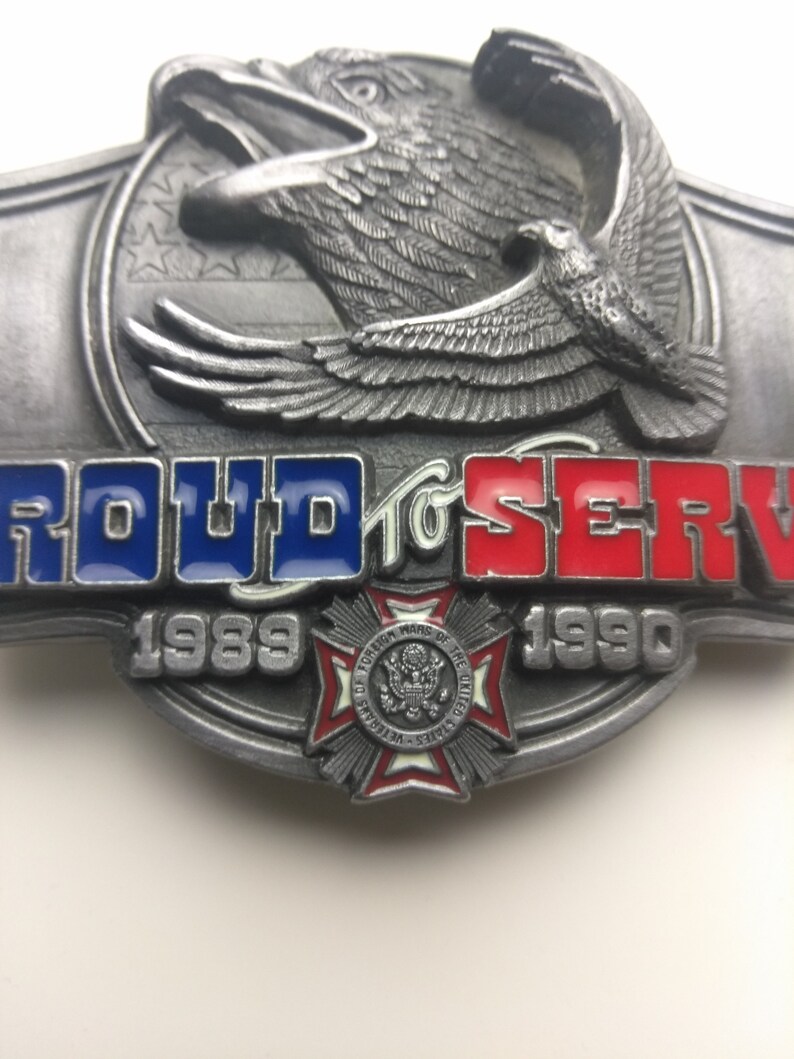 May include: A silver belt buckle with a bald eagle design and the words "Proud to Serve" in red, white, and blue. The buckle also features a red, white, and blue cross with the words "Foreign Wars of the United States" and the years "1989" and "1990".