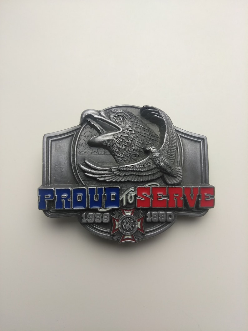 May include: A silver belt buckle with an eagle design and the words "Proud to Serve 1989-1990".