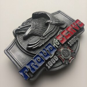 May include: A silver belt buckle with a bald eagle design and the words "Proud to Serve 1989-1990". The buckle also features a red, white, and blue American flag design and a small red, white, and blue emblem with the words "Veterans of the United States of America".