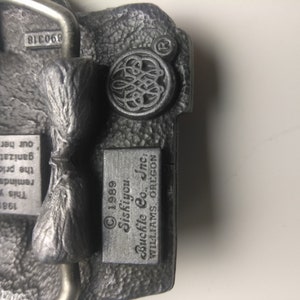 May include: A silver belt buckle with a Siskiyou Buckle Co., Inc. logo and the text "1989 Siskiyou Buckle Co., Inc. WILLIAMS, OREGON".