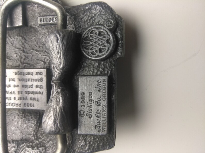 May include: A silver belt buckle with a Siskiyou Buckle Co., Inc. logo and the text "1989 Siskiyou Buckle Co., Inc. WILLIAMS, OREGON".