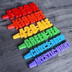 May include: A rainbow of colorful wooden signs with different words on them. The words are "FRESH", "KISMET", "428-ALE", "GREEN TEA", "CODY'S BREW", and "MYSTIC NIGHT".