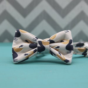 May include: A white bow tie with a pattern of yellow birds and fish. The bow tie is made of fabric and has a classic bow shape.