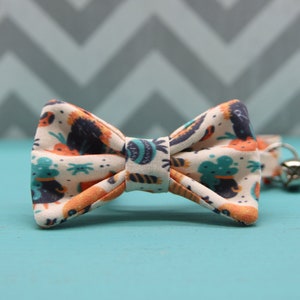 May include: A white bow tie with a colorful pattern of orange, blue, and black. The pattern features a variety of abstract shapes and designs.