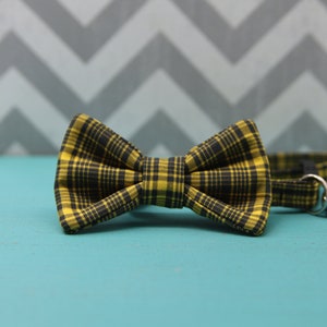 May include: A yellow and black plaid bow tie. The bow tie is made of fabric and has a classic bow shape.